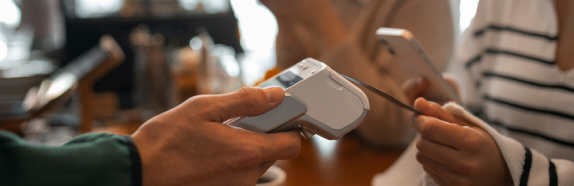 Pessoa com uma maquininha recebendo o pagamento de uma cliente